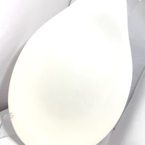 May include: A white, teardrop-shaped ceramic serving platter. The platter has a smooth, matte finish and is displayed on a clear stand against a white background. The design is simple and elegant, suitable for various culinary presentations.