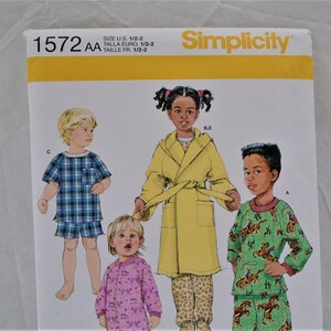 May include: Simplicity sewing pattern 1572 AA for sizes 1/2-2. The pattern includes instructions for making pajamas for children. The image shows four children wearing different styles of pajamas, including a plaid pajama set, a yellow robe, a pink pajama set, and a green and brown pajama set.