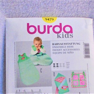 May include: Burda Kids sewing pattern number 9479 for baby clothes. The pattern includes instructions for a sleeping bag, a swaddle blanket, and a baby quilt. The pattern is illustrated with a baby wearing the sleeping bag and a close-up of the finished items.