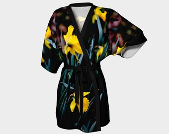 Puede incluir: Una bata de kimono negra con estampado floral de narcisos amarillos sobre un fondo oscuro. La bata tiene un cinturón de atar y mangas cortas.