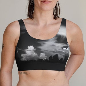 May include: A black sports bra with a black and white photo print of a cloudy sky and trees. The bra has a scoop neck and thin straps.