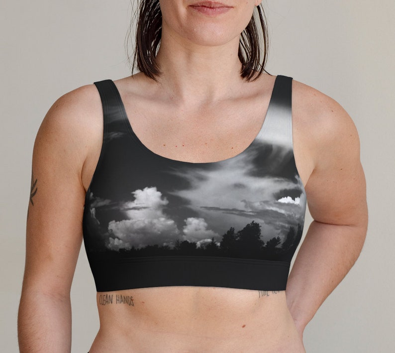 May include: A black sports bra with a black and white photo print of a cloudy sky and trees. The bra has a scoop neck and thin straps.