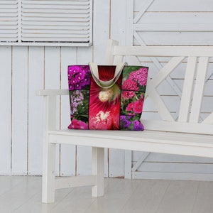 May include: A white canvas tote bag with a colorful floral print featuring pink, purple, and white flowers. The bag has two handles and is sitting on a white bench.