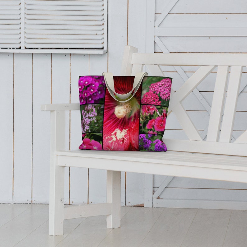 May include: A white canvas tote bag with a colorful floral print featuring pink, purple, and white flowers. The bag has two handles and is sitting on a white bench.