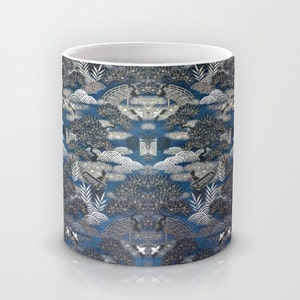 May include: A white ceramic mug with a blue and silver pattern of stylized trees, clouds, and bridges. The pattern is repeated across the entire mug.
