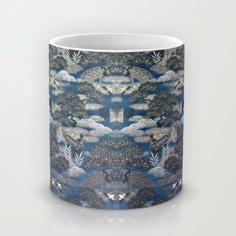 May include: A white ceramic mug with a blue and silver pattern of stylized trees, clouds, and bridges. The pattern is repeated across the entire mug.
