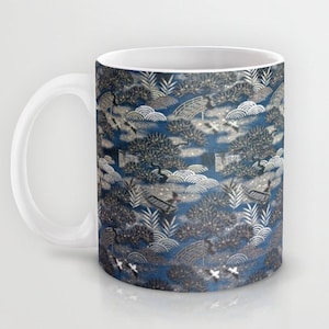 Op de afbeelding: Een witte keramische mok met een blauw en zilveren patroon van gestileerde bomen, wolken en bruggen. Het patroon wordt over de hele mok herhaald.