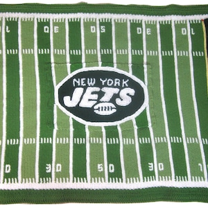 Könnte beinhalten: Grüne und weiße gestrickte Decke mit einem Fußballfeld-Design und dem New York Jets Logo in der Mitte.