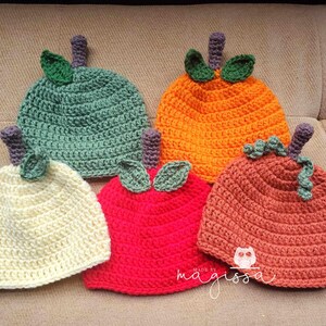 May include: Five crocheted pumpkin hats in different colors, including green, orange, cream, red, and brown. The hats are all made with a similar stitch pattern and have a small leaf detail on top.