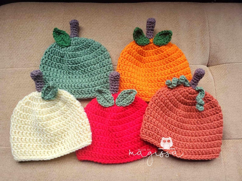 May include: Five crocheted pumpkin hats in different colors, including green, orange, cream, red, and brown. The hats are all made with a similar stitch pattern and have a small leaf detail on top.