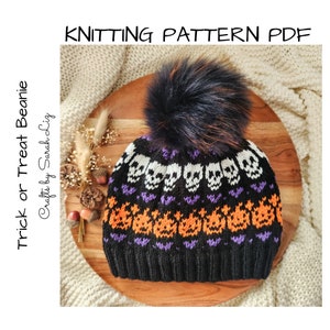 May include: A black and orange knitted beanie with a skull and pumpkin pattern. The beanie has a black faux fur pom pom on top. The beanie is on a wooden surface. The text "Trick or Treat Beanie" and "Crafts by Sarah Liz" is on the left side of the image.