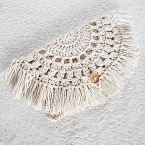 May include: A crocheted cream-colored shawl with a fringe border and a wooden button.