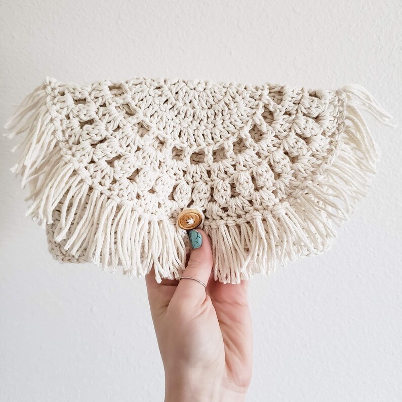 May include: A crocheted clutch bag with a fringe border and a gold button closure.