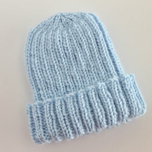 May include: A light blue knitted beanie hat. The hat has a ribbed texture and a folded brim.