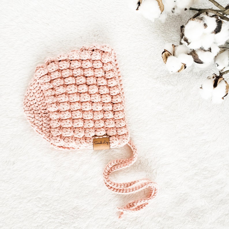 May include: A pink crocheted baby bonnet with a brown leather tag that says "Such Big"