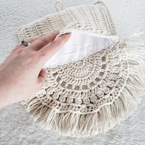 May include: A crocheted bag with a white lining and a fringe border. The bag is made of natural fibers and has a simple, elegant design.