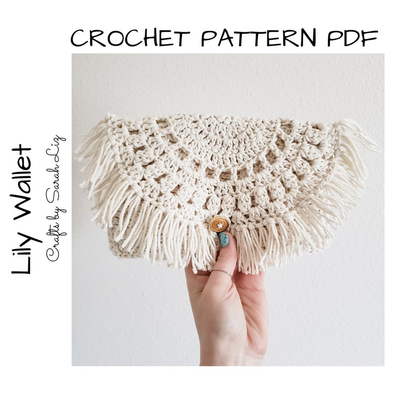 May include: A crocheted cream-colored wallet with a fringe border and a button closure. The wallet is held in a hand. The text "Lily Wallet Crafts by Sarah Lizg" is on the left side of the image.