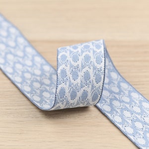 Puede incluir: Una banda elástica azul y blanca con estampado. La banda está tejida con un patrón repetitivo de círculos blancos sobre un fondo azul claro.