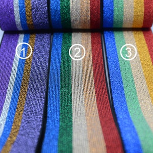 Puede incluir: Tres colores diferentes de ribete elástico con un patrón de rayas doradas, plateadas y blancas metálicas. El ribete se muestra en morado, azul y rojo.