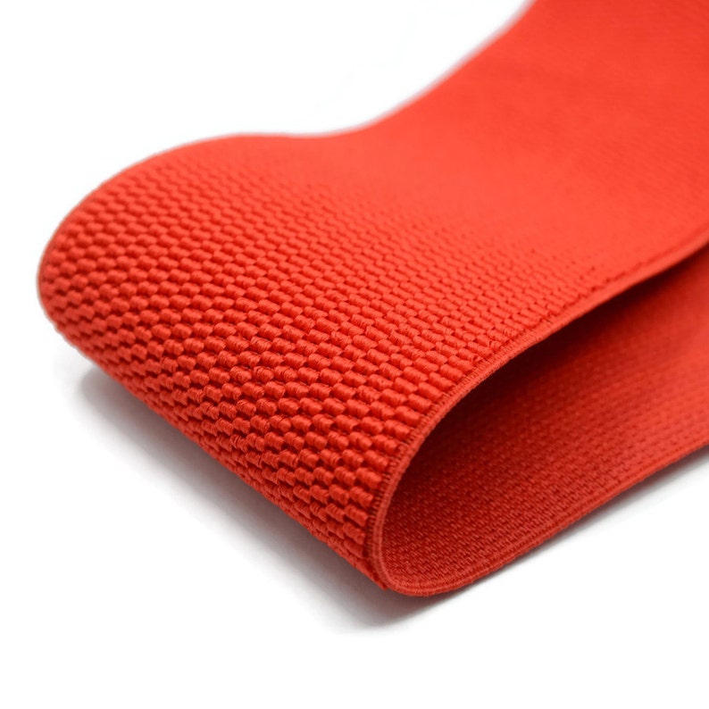 May include: Red elastic band with a textured surface. The band is folded in half, showing the inside and outside of the material.