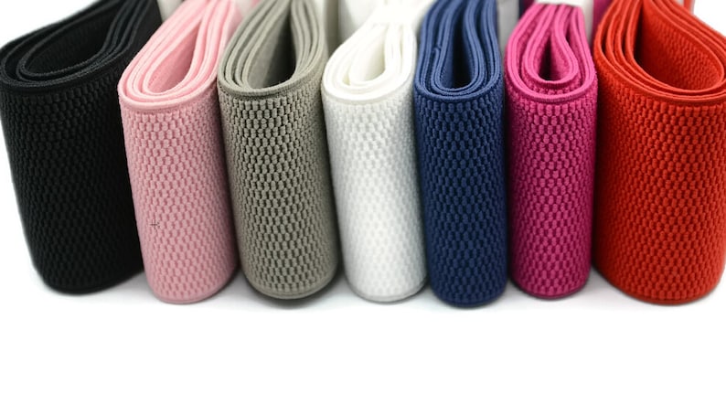 May include: Assortment of eight elastic bands in various colours, including black, pink, grey, white, blue, red, and orange. The bands are all the same width and have a textured surface.