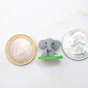 Miniatur Elefant aus Polymerclay, sitzend auf grünem Untergrund Vergleich mit Euro und Quarter