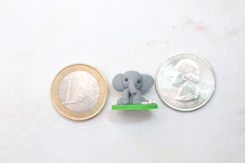 Miniatur Elefant aus Polymerclay, sitzend auf grünem Untergrund Vergleich mit Euro und Quarter
