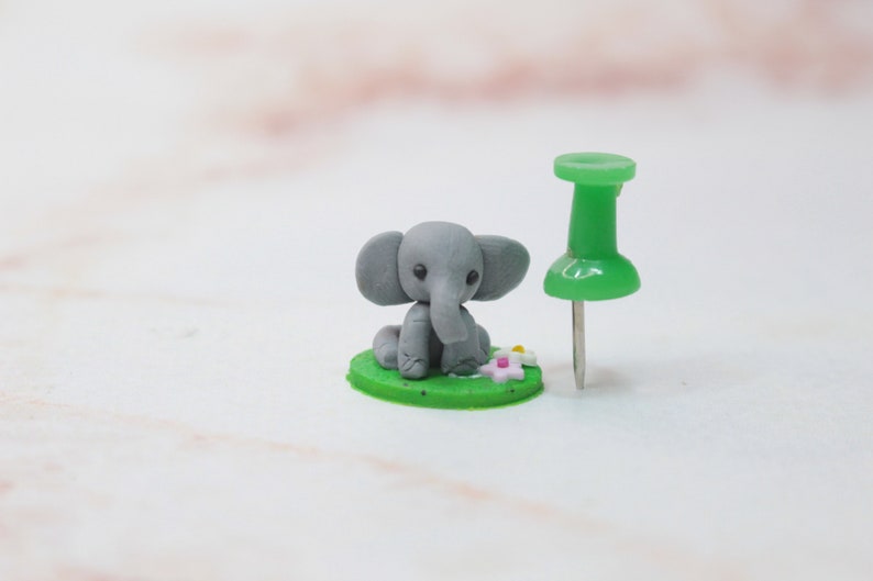 Größenvergleich mit Pin, Miniatur Elefant aus Polymerclay, sitzend auf grünem Untergrund