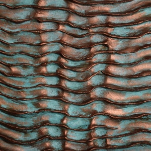 Puede incluir: Primer plano de una superficie texturizada con un patr&oacute;n ondulado. La superficie es una mezcla de colores turquesa y cobre.