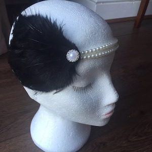 May include: A black feather headband with a pearl and rhinestone embellishment.