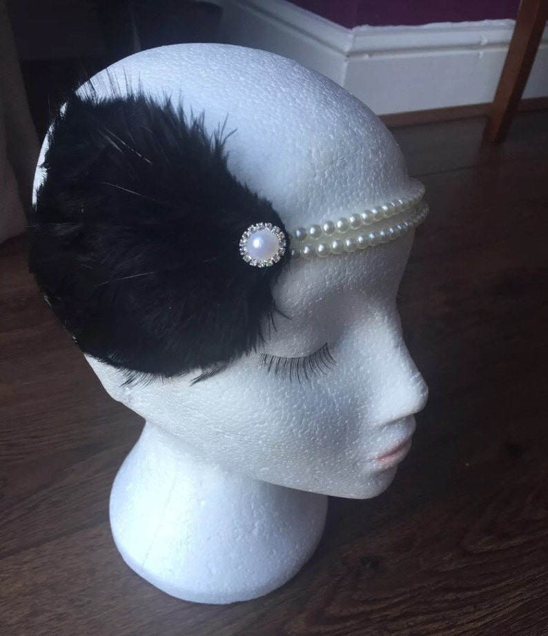 May include: A black feather headband with a pearl and rhinestone embellishment.
