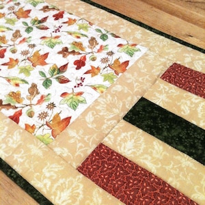 Pu&ograve; includere: Un runner da tavola trapuntato con un pannello centrale su sfondo bianco stampato con foglie autunnali colorate, ghiande e bacche. Il bordo &egrave; composto da strisce alternate di tessuto color cuoio con motivo a foglie, verde scuro e rosso.