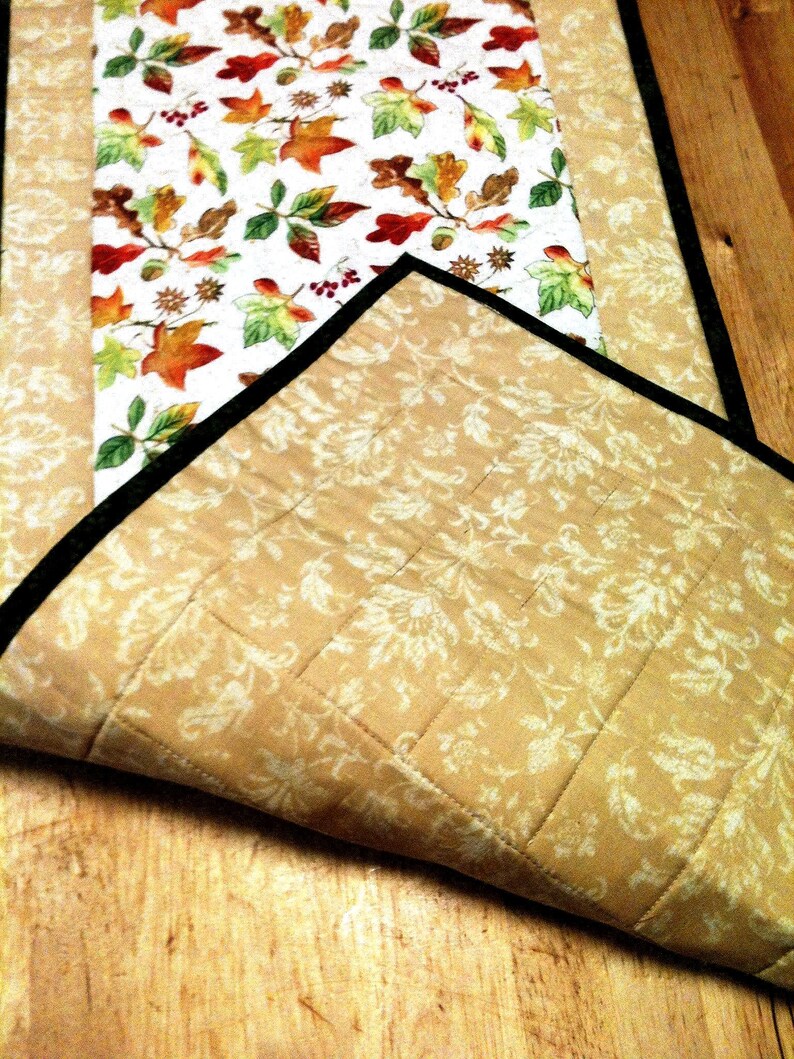 Pu&ograve; includere: Un runner da tavola trapuntato con un pannello centrale su sfondo bianco e un motivo colorato di foglie autunnali. I pannelli laterali sono in tessuto color cuoio con una stampa damascata floreale color crema. Il bordo &egrave; rifinito in nero.