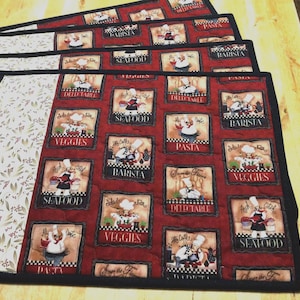 May include: A set of rectangular quilted placemats featuring a red background with repeating square panels depicting chefs and food labels like Seafood, Veggies, Pasta, and Barista. A side panel displays a cream fabric with a brown leaf pattern.