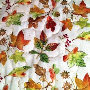 Pu&ograve; includere: Un tessuto trapuntato con sfondo color crema e un motivo ripetitivo di foglie autunnali nei toni dell'arancione, rosso, giallo e verde, intervallato da piccoli grappoli di bacche rosse e ghiande marroni, rifinito con cuciture ondulate.