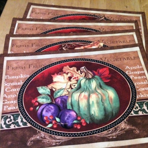 May include: Set of four brown placemats with a red, green, and white design featuring a pumpkin, grapes, pears, and squash. The placemats have the text "Fresh Fruit" and "Vegetables" printed on them.