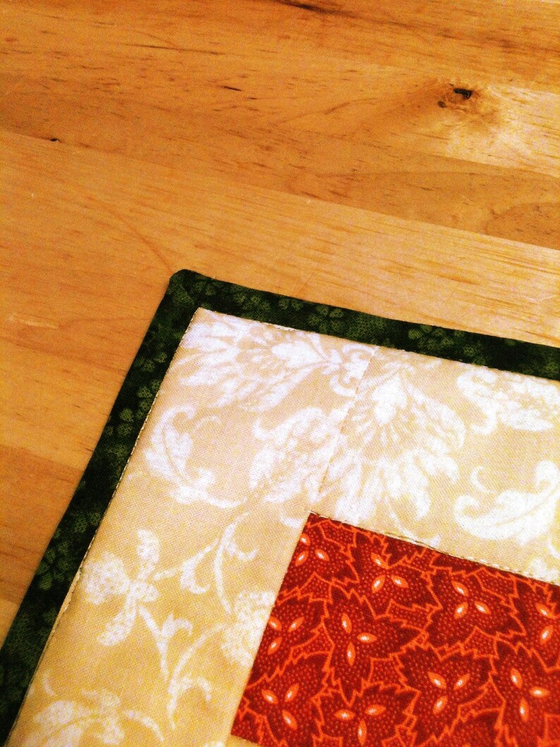 Pu&ograve; includere: Un pezzo di tessuto trapuntato caratterizzato da un bordo verde scuro con un sottile motivo floreale, una sezione color crema con una stampa damascata bianca e un blocco centrale di tessuto rosso scuro decorato con un motivo ripetuto di piccole foglie arancioni.