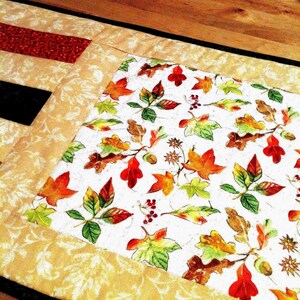 Pu&ograve; includere: Un runner da tavola rettangolare in tessuto con un pannello centrale su sfondo bianco stampato con foglie autunnali colorate, ghiande e bacche. Il pannello &egrave; bordato da un tessuto color cuoio con un sottile motivo a foglie color crema.
