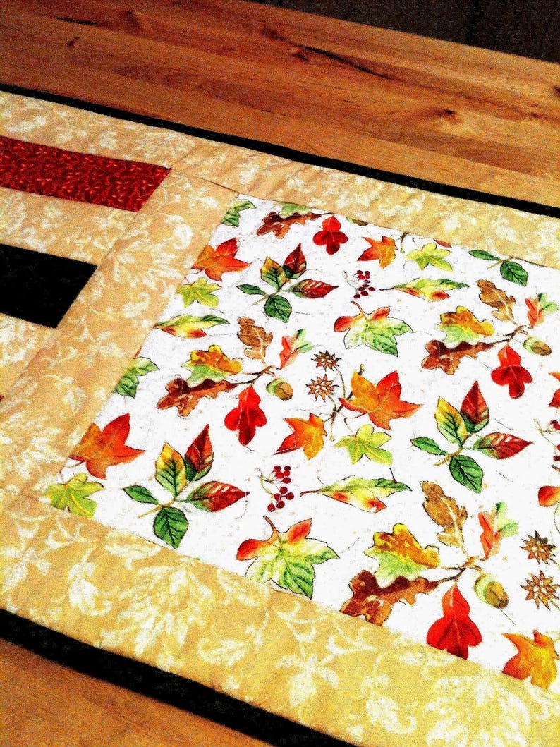 Pu&ograve; includere: Un runner da tavola rettangolare in tessuto con un pannello centrale su sfondo bianco stampato con foglie autunnali colorate, ghiande e bacche. Il pannello &egrave; bordato da un tessuto color cuoio con un sottile motivo a foglie color crema.