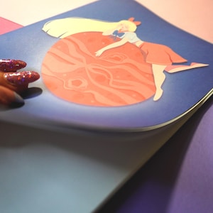 Può includere: Una stampa illustrata blu e rosa di un personaggio dei cartoni animati che tiene un grande globo rosa. Il personaggio ha i capelli biondi, una gonna rossa e scarpe bianche.