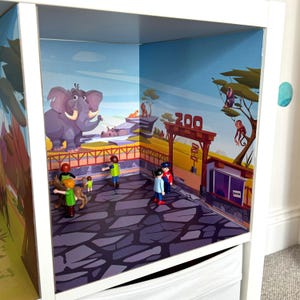 May include: A miniature zoo playset with a colourful backdrop featuring an elephant, a giraffe, and a monkey. The set includes small plastic figures of people and animals. The zoo entrance has a sign that reads "Zoo".