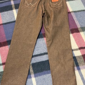 May include: Brown Wrangler jeans with white stitching on the back pockets and a brown leather patch. The jeans have a classic five-pocket design and a straight leg cut. The Wrangler logo is visible on the back pocket.