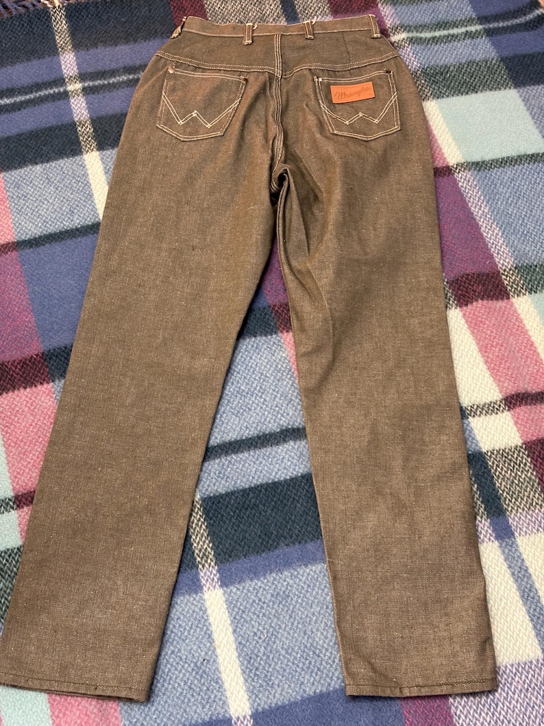 May include: Brown Wrangler jeans with white stitching on the back pockets and a brown leather patch. The jeans have a classic five-pocket design and a straight leg cut. The Wrangler logo is visible on the back pocket.