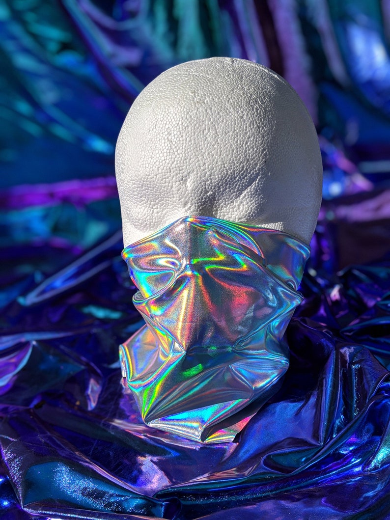 Silver holographic neck gaiter is wrapped around a white mannequin head reflecting rainbow colors from light shining on it.