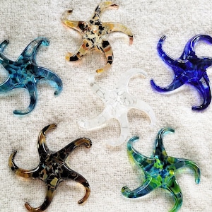 May include: Six glass starfish ornaments in various colors and patterns. The starfish are made of clear, blue, white, and brown glass. They are all about 4 inches in size.