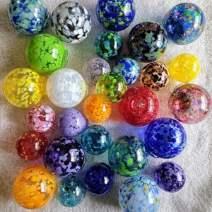 May include: A collection of colorful glass marbles with various patterns and textures. The marbles are arranged in a random pattern on a white fabric surface.