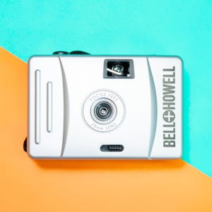 May include: A silver camera with a black lens and the text "FOCUS FREE 28mm LENS" and "BELLO+HOWELL" on the side.
