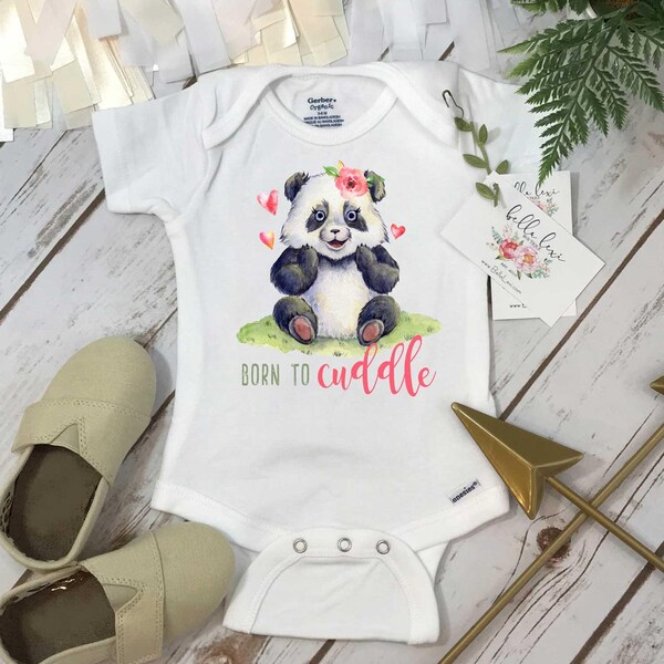 May include: A white short-sleeved baby bodysuit featuring a watercolor illustration of a panda sitting on green grass with pink hearts and a flower on its head. The text "BORN TO cuddle" is printed below the panda in green and pink script.