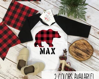 Op de afbeelding: Een wit raglan-shirt met zwarte driekwartmouwen, voorzien van een rood-zwart geruite berensilhouet en de naam MAX in het zwart gedrukt. Het shirt bevat een wit label met bloemendetails en tekst.
