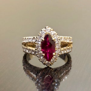 May include: A gold ring with a large, red, marquise-shaped gemstone surrounded by smaller, white gemstones.